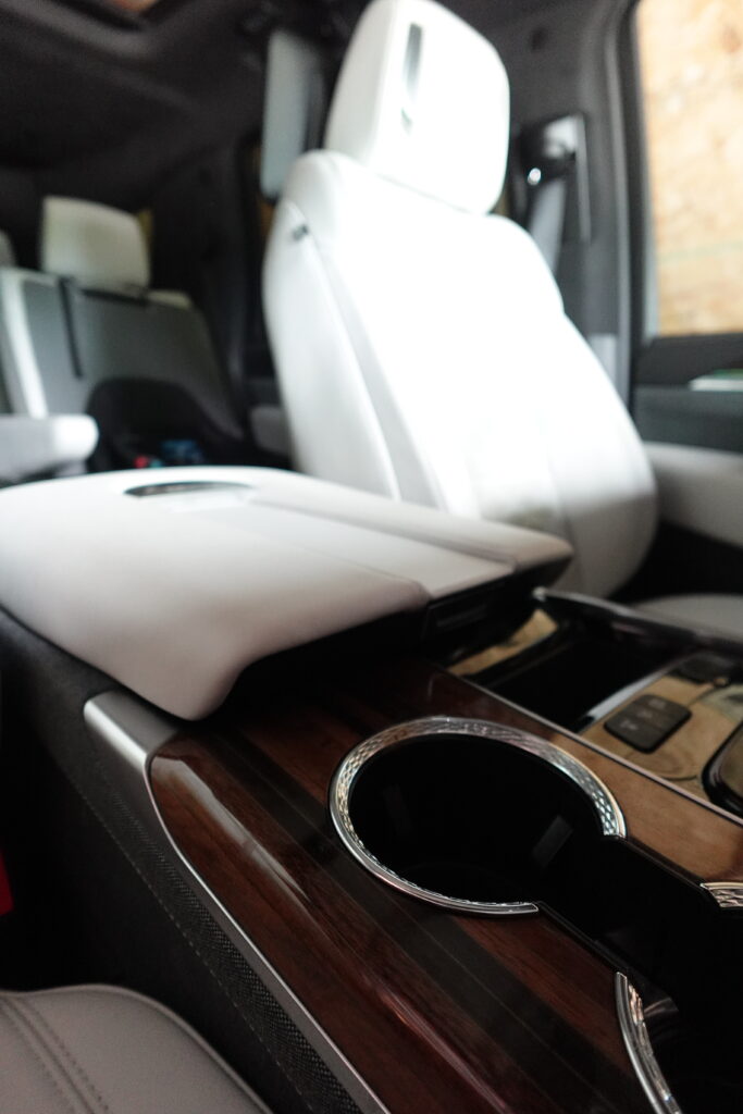 Detailed luxury SUV interior with clean wood trim, cupholder, and white leather seats.