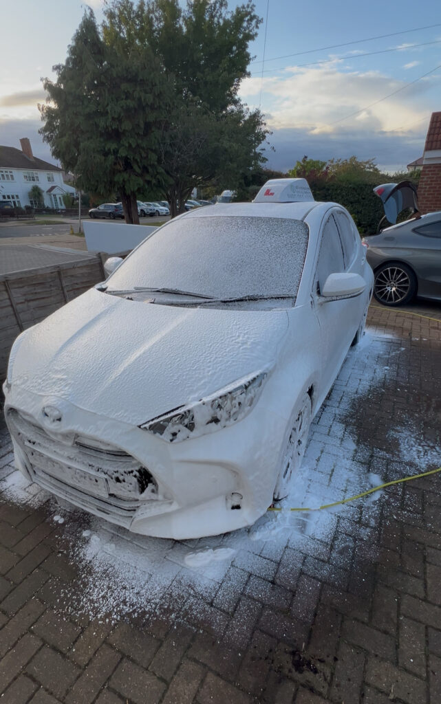 Car covered in thick snow foam during the pre-wash stage of a full exterior detail.